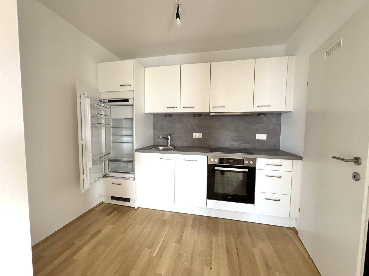 Moderne, kompakte Einbauküche mit weißen Schränken, integriertem Kühlschrank und Holzboden.