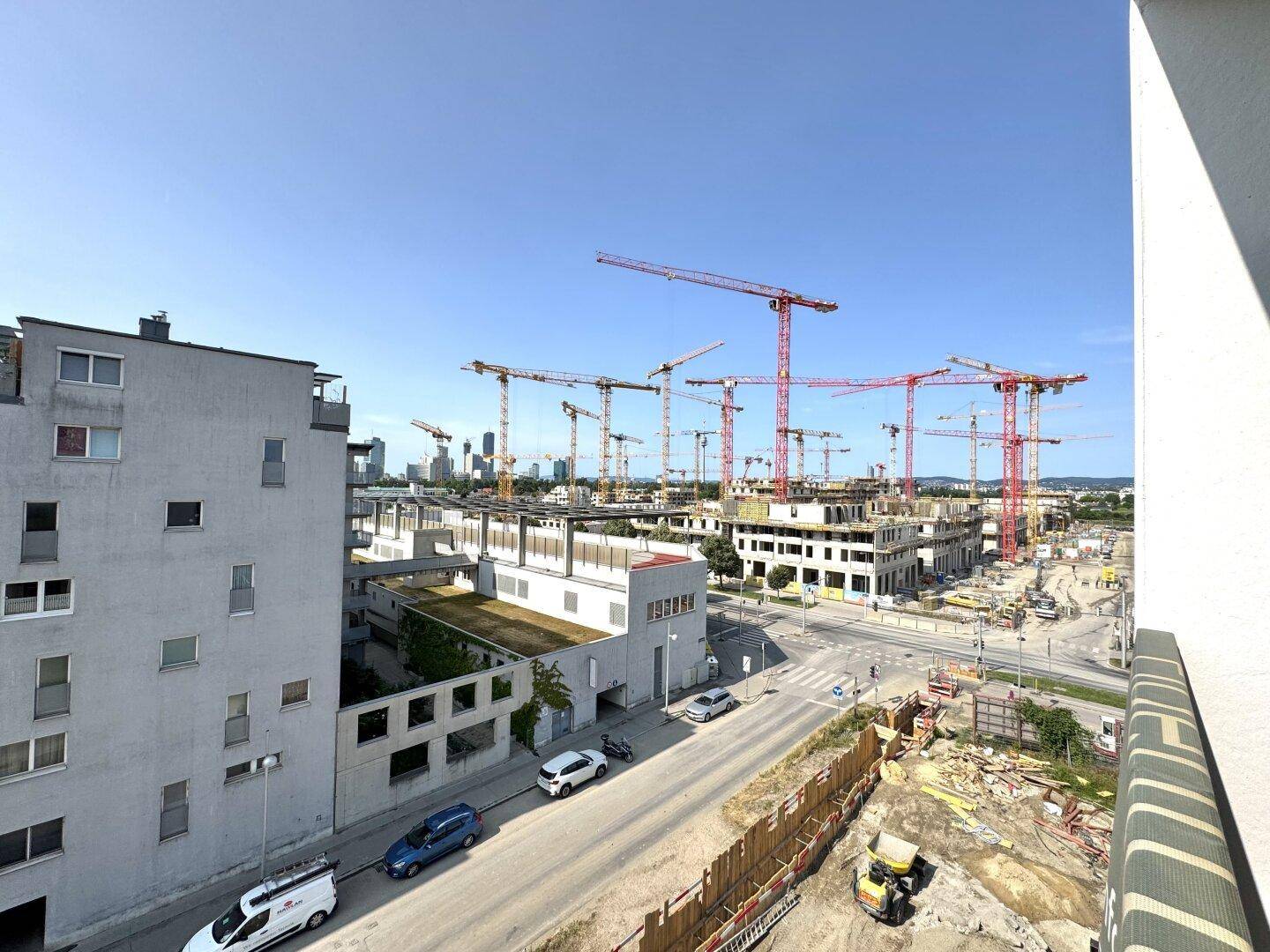 Blick von einem Balkon auf eine große Baustelle mit vielen Kränen und neuen Gebäuden in der Ferne.