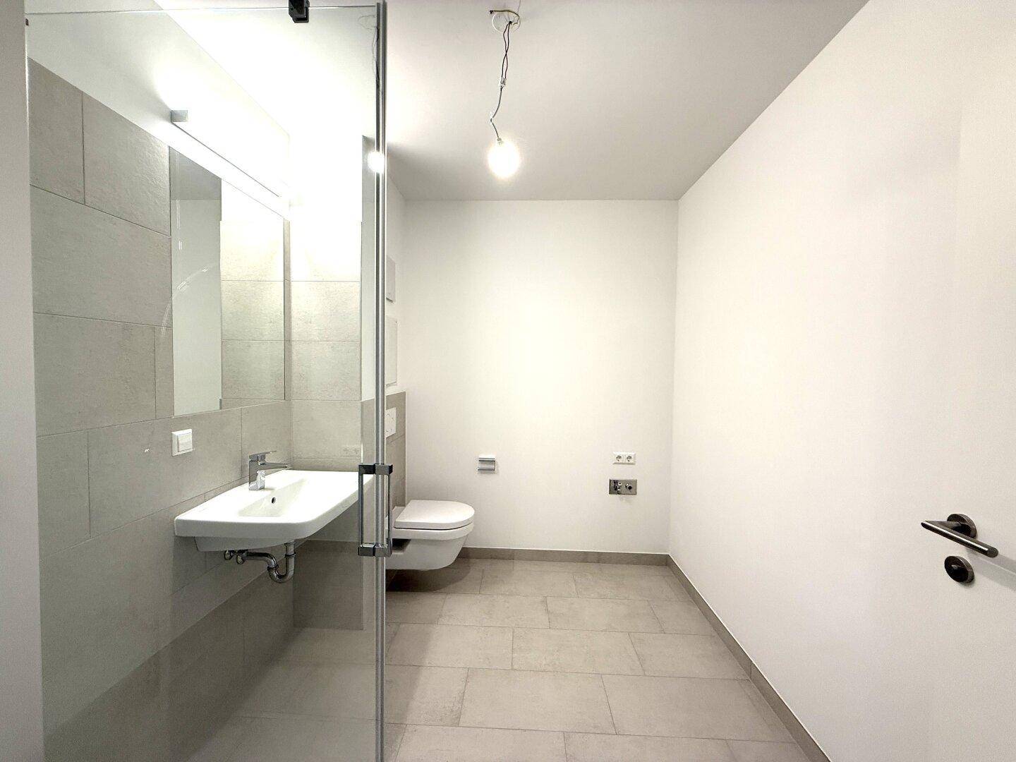 Modernes Badezimmer mit Dusche, wandhängendem WC und Waschbecken, in hellen Fliesen gehalten.