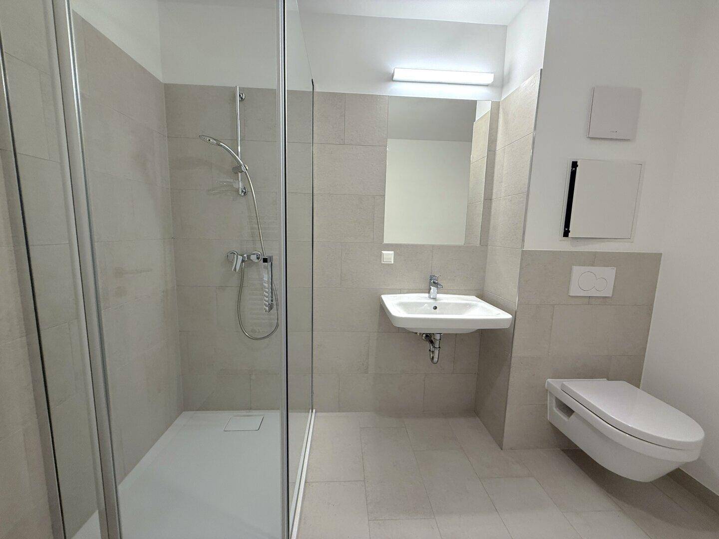Zeitgemäßes Badezimmer mit ebenerdiger Dusche, wandhängendem WC und integriertem Spiegel.