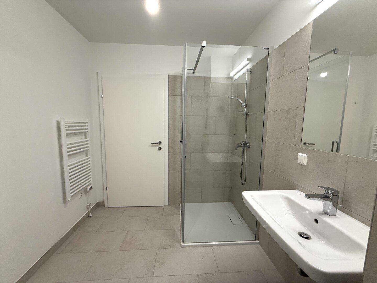 Helles Badezimmer mit Dusche, Waschbecken und beheiztem Handtuchhalter, in neutralen Farben.