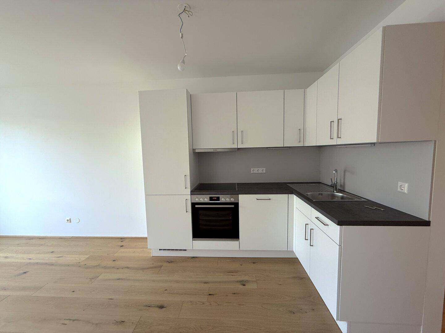 Moderne Küchenzeile mit weißen Schränken, dunkler Arbeitsplatte und integriertem Backofen.