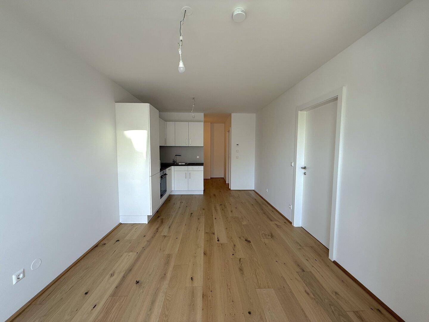 Geräumiger Wohnbereich mit offener Küchenzeile und hellem Parkettboden, ideal für modernes Wohnen.