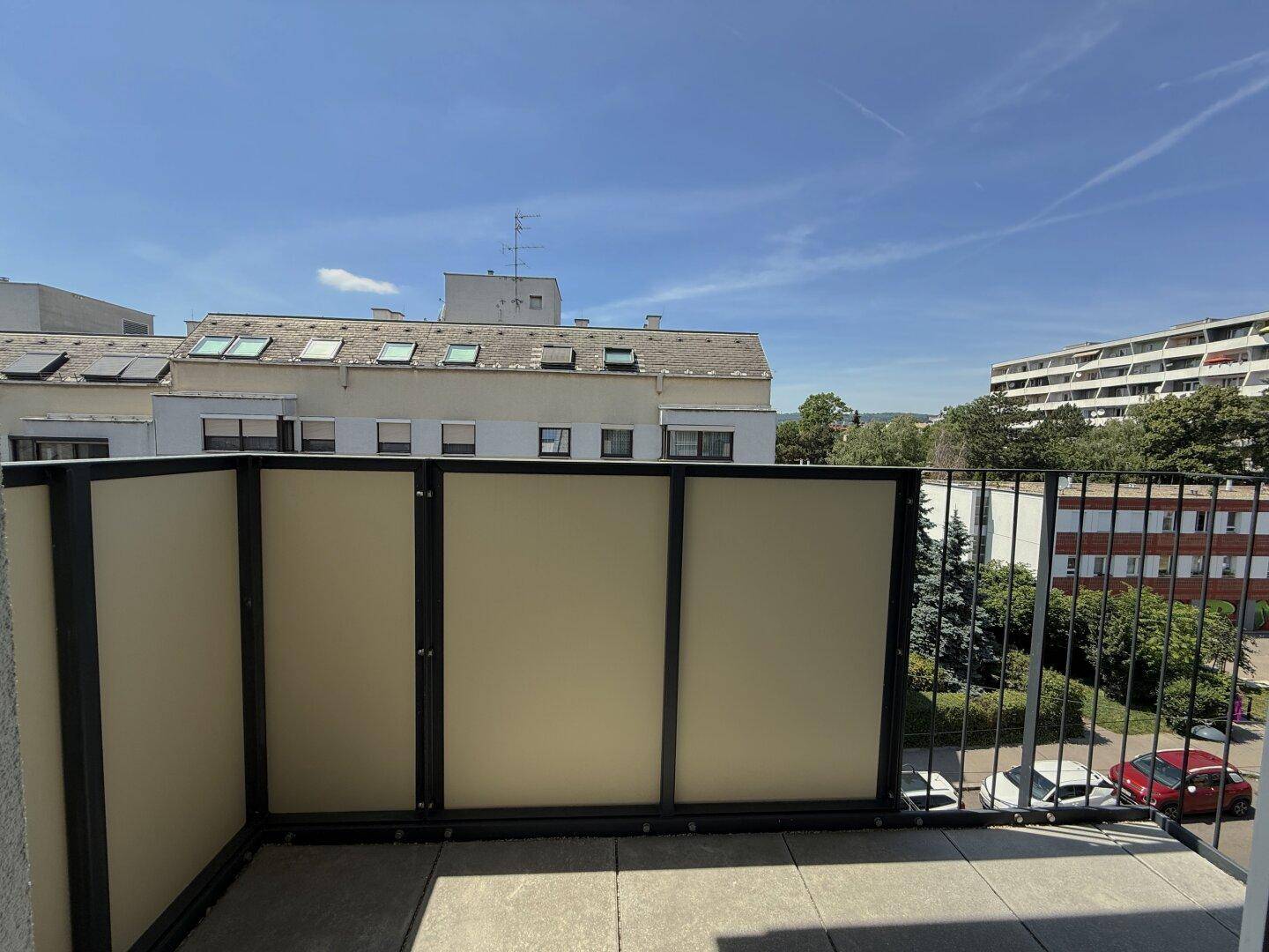 Sonniger Balkon mit Sichtschutz und Blick auf die umliegenden Gebäude und Grünflächen.