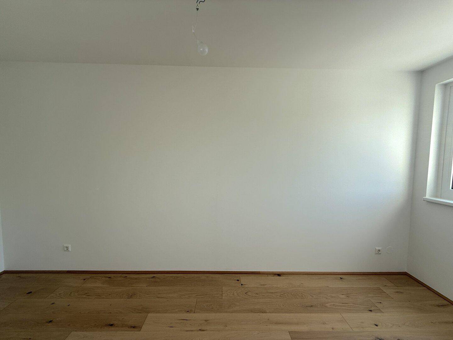 Heller Raum mit Parkettboden und einer großen Wandfläche, ideal für Möbelplatzierung.