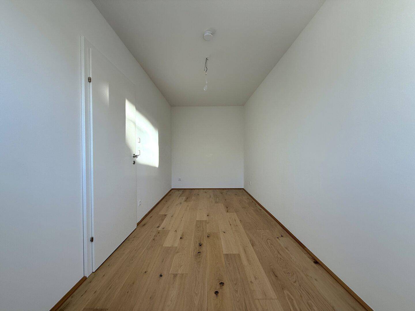Leeres Zimmer mit hellem Parkettboden und weiß gestrichenen Wänden, bereit zur individuellen Gestaltung.