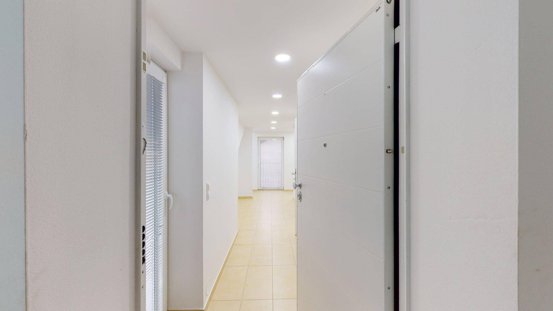 Geräumiger Flur mit heller Fliesenboden, weißen Wänden und moderner Deckenbeleuchtung.