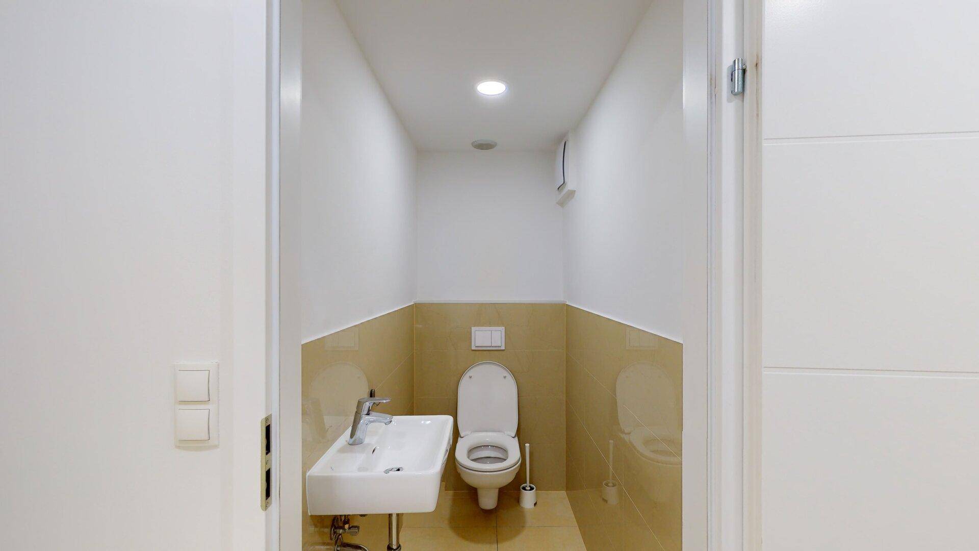 Kleines Gäste-WC mit modernem Waschbecken, Wand-WC und beigefarbenen Fliesen an Wänden und Boden.