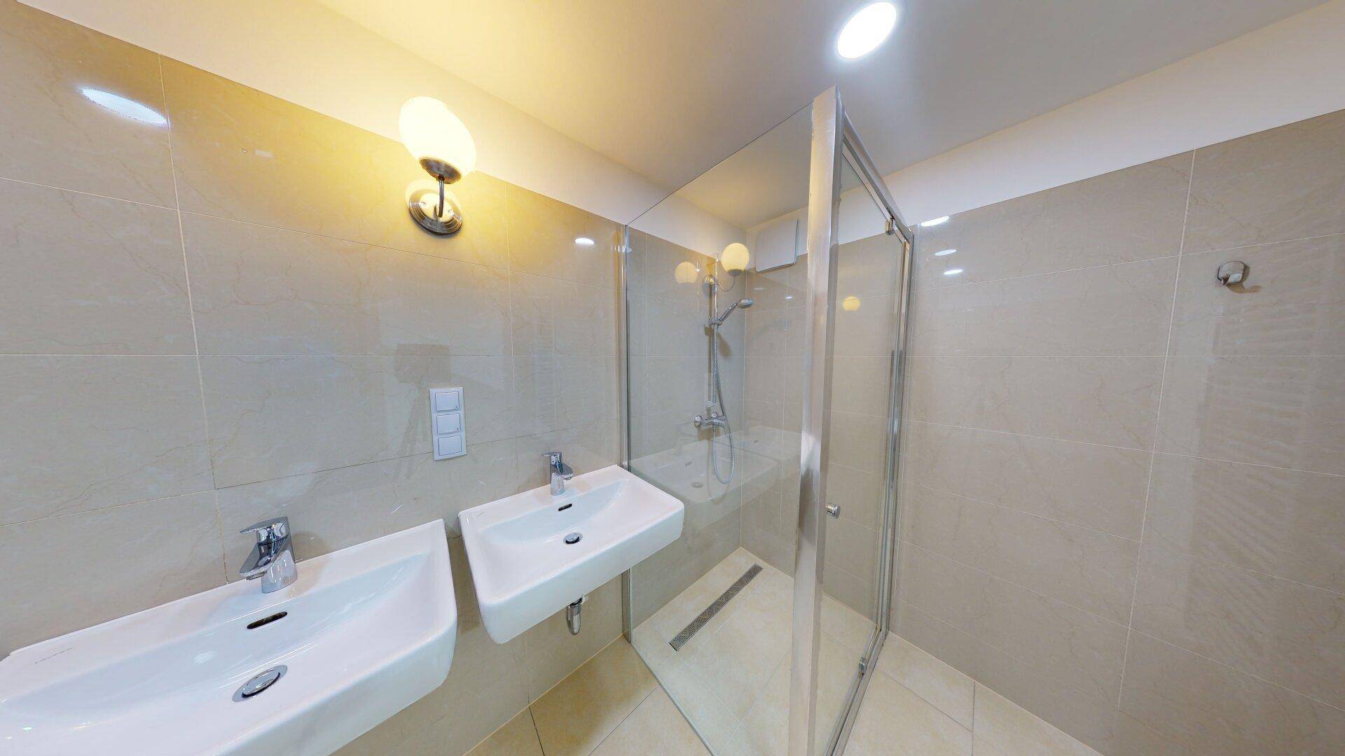 Modernes Badezimmer mit zwei Waschbecken und einer geräumigen begehbaren Dusche, hell gefliest.