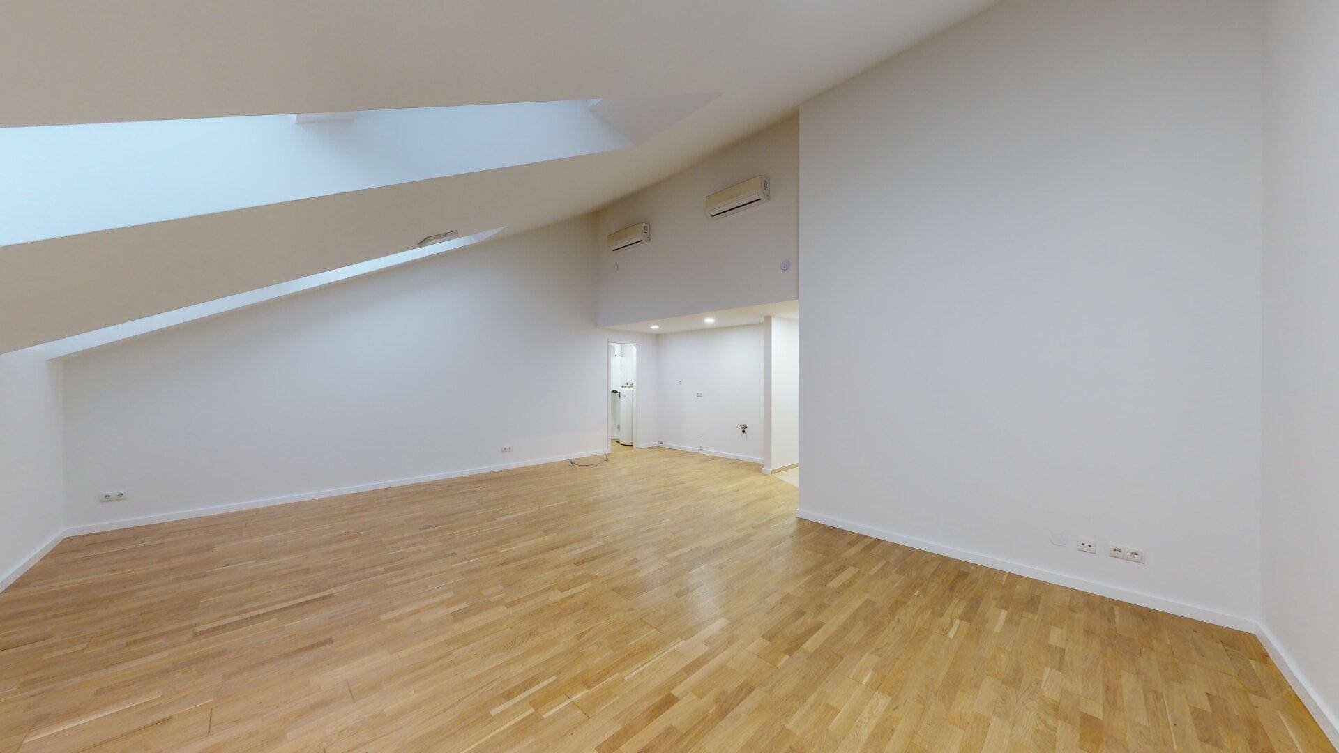 Heller Dachgeschossraum mit Holzfußboden, schrägen Wänden und installierter Klimaanlage.