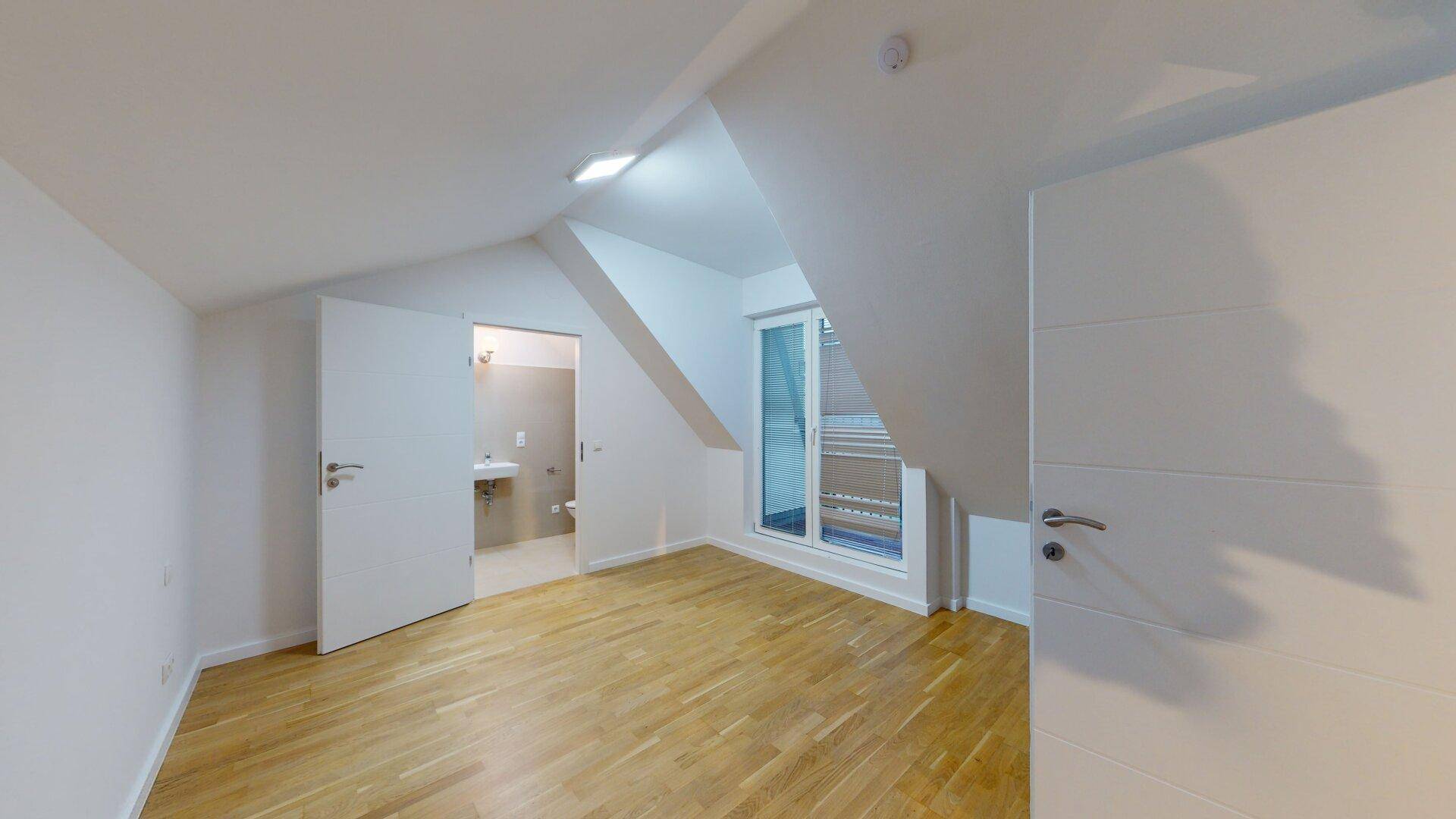 Helles Schlafzimmer mit Holzfußboden, Dachschrägen und Zugang zu einem Badezimmer und Balkon.