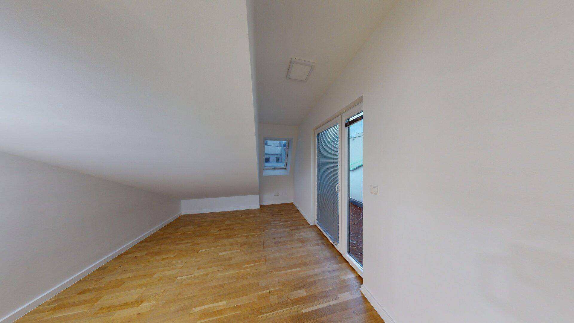 Heller Dachgeschossraum mit Holzfußboden, schrägen Wänden und Zugang zu einem Außenbereich.