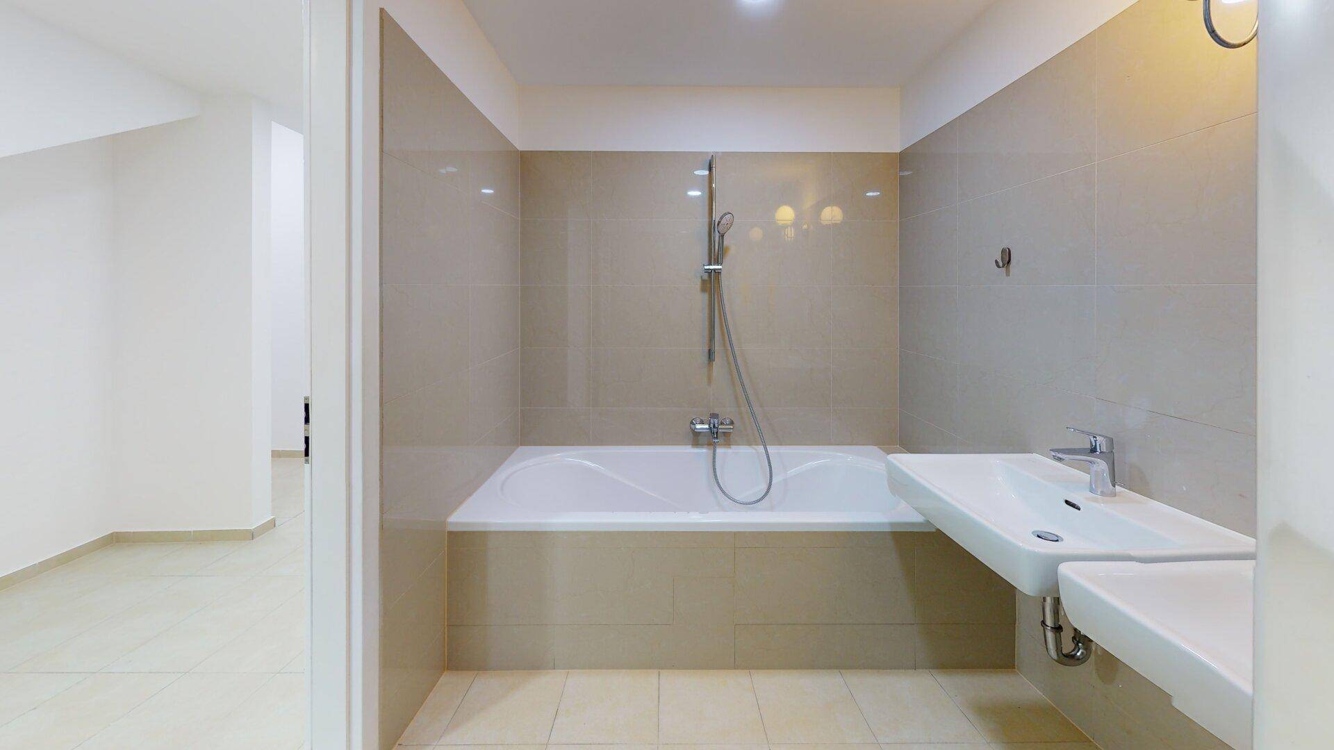 Modernes Badezimmer mit Badewanne, Duscharmatur und einem einzelnen Waschbecken, hell gefliest.