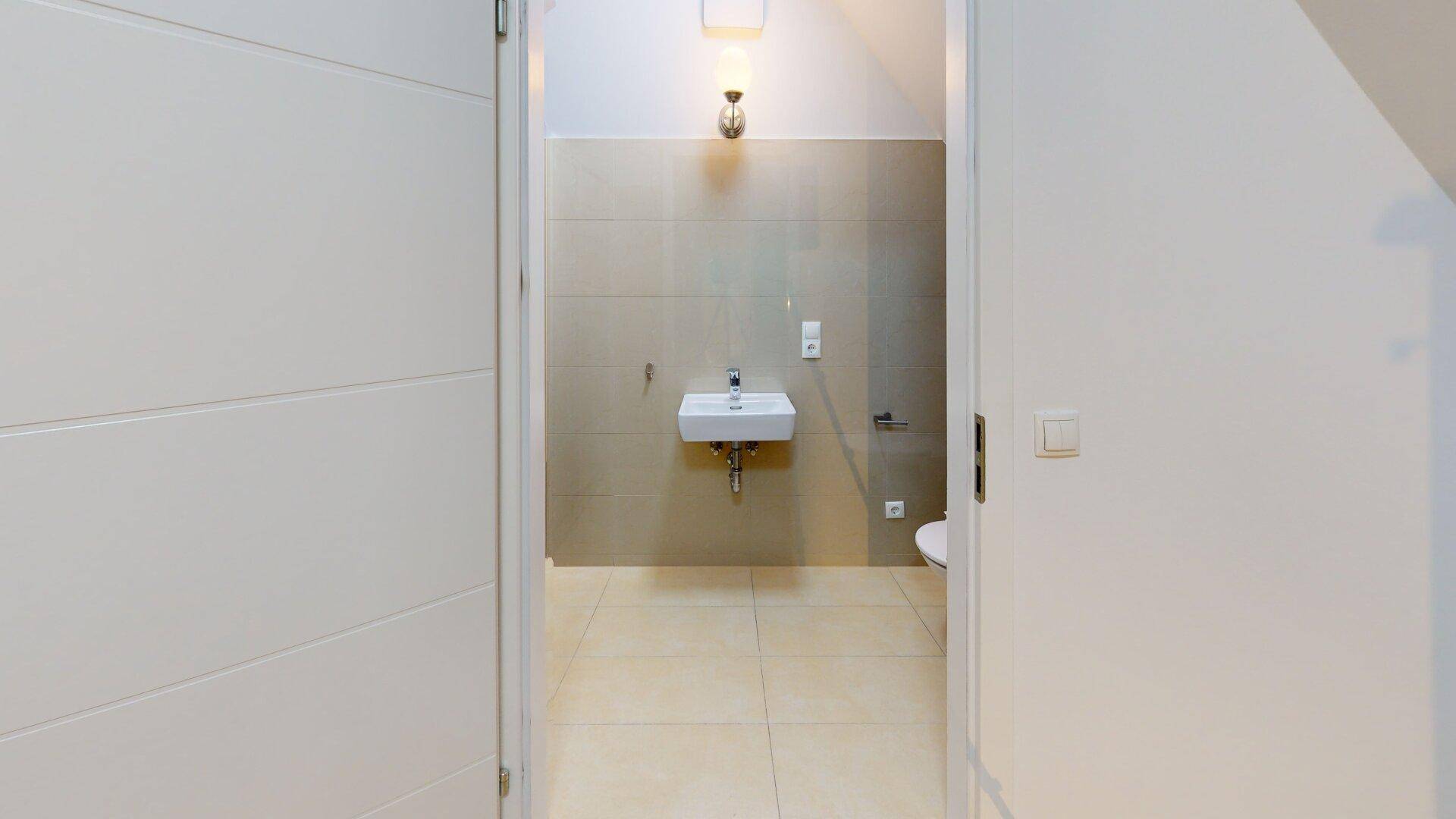 Kleines WC mit Waschbecken und Toilette, durch eine Tür vom Flur aus zugänglich, mit Dachschräge.
