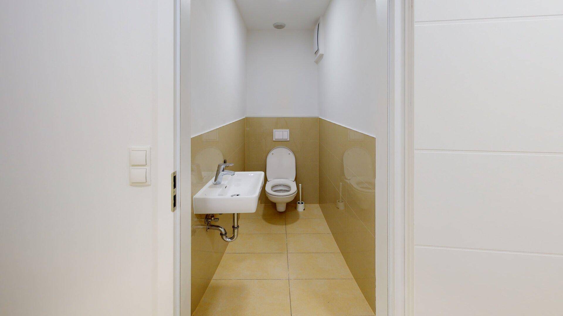 Kompaktes Gäste-WC mit Toilette und kleinem Waschbecken, hell gefliest und funktional eingerichtet.