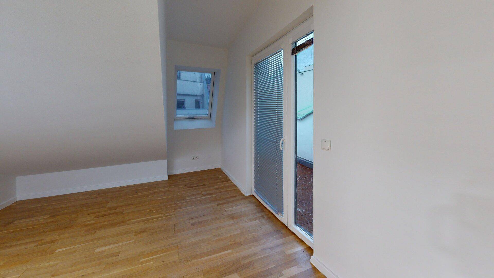 Helles Schlafzimmer mit Holzboden, Dachschräge und großem Fenster mit Zugang zu einem Außenbereich.