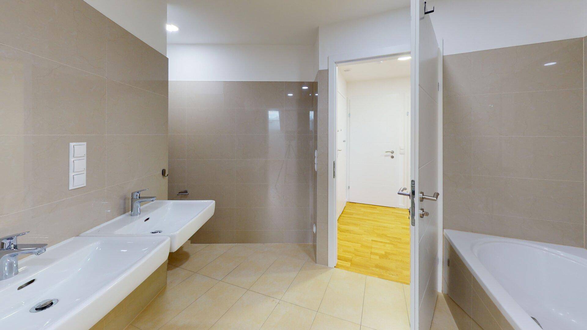 Modernes Badezimmer mit Doppelwaschbecken, Badewanne und hellen Fliesen an Wänden und Boden.