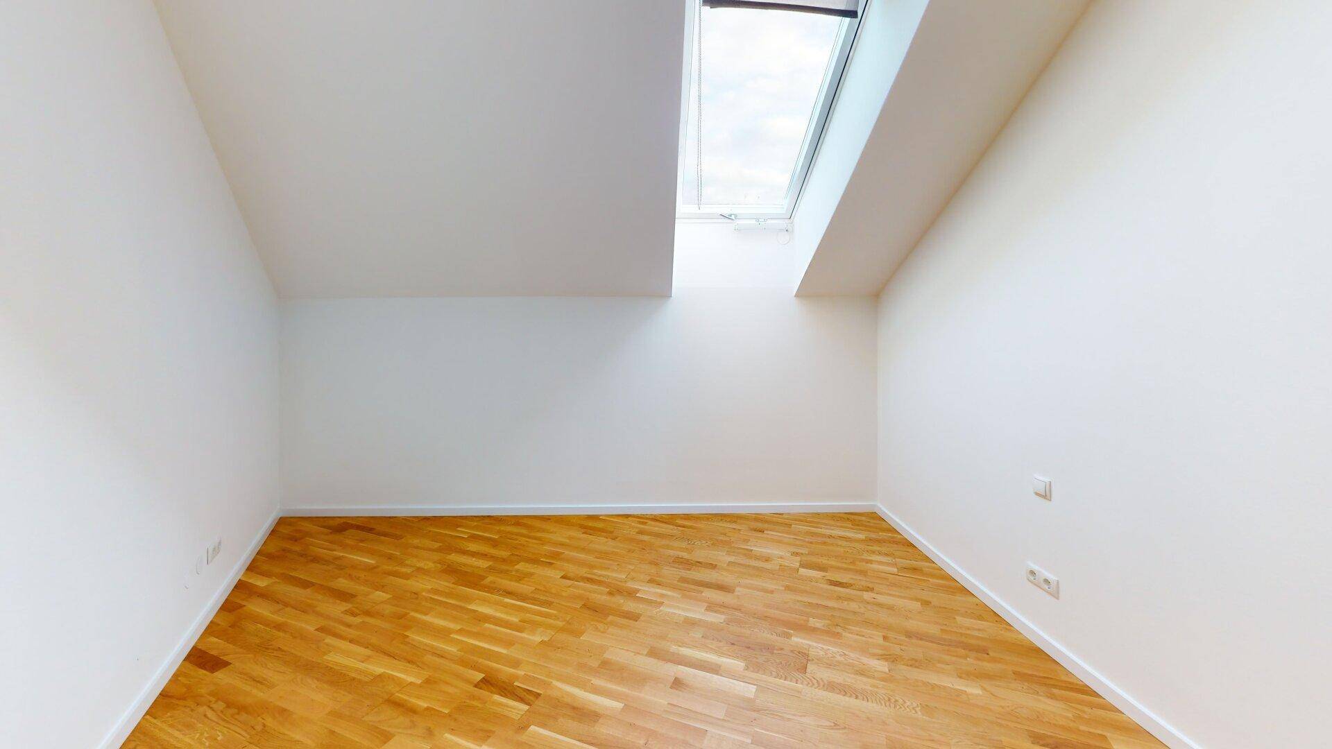 Helles Zimmer mit Holzboden, weiß gestrichenen Wänden und einem Dachfenster für Tageslicht.