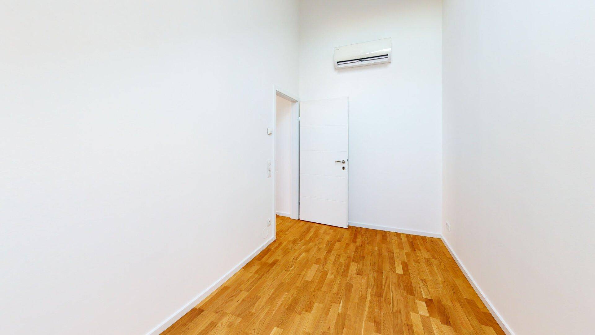 Kleineres Zimmer mit Holzboden, weißen Wänden und installierter Klimaanlage für Komfort.