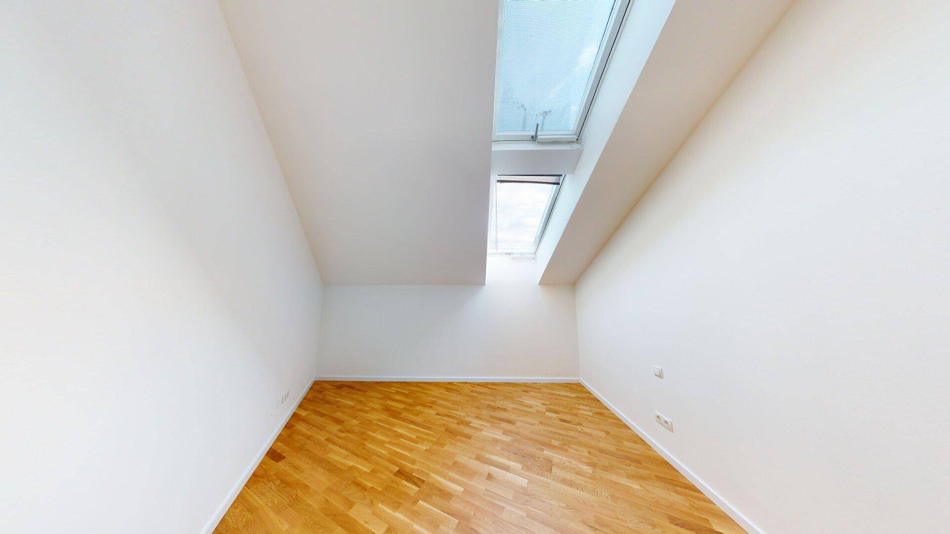Helles Zimmer mit Holzboden, weißen Wänden und einem Dachfenster für Tageslicht.