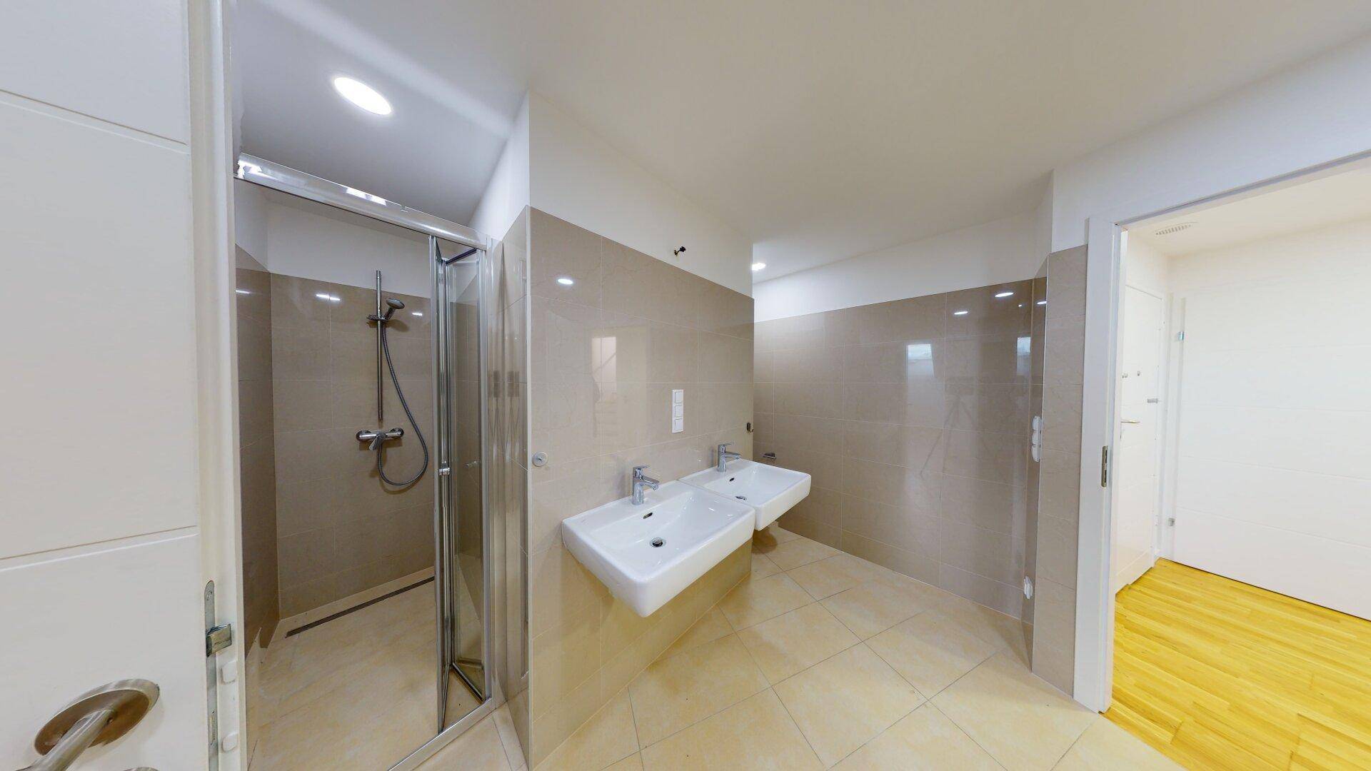 Modernes Badezimmer mit Doppelwaschbecken, Duschkabine und hellen Fliesen an Wänden und Boden.