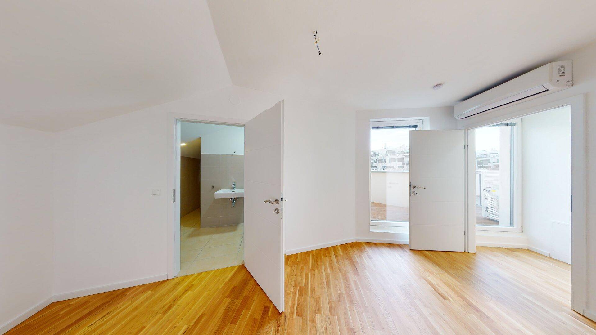 Schlafzimmer mit Holzboden, Klimaanlage und Zugang zu einem Balkon sowie einem Badezimmer.