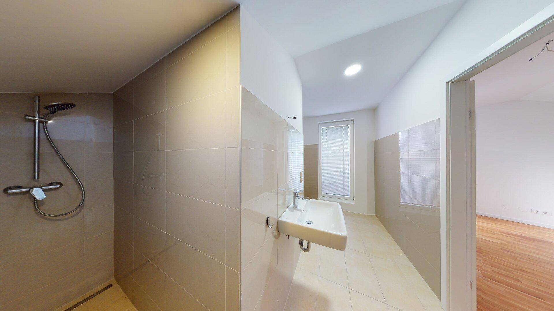 Modernes Badezimmer mit Einzelwaschbecken, Dusche und hellen Fliesen an Wänden und Boden.