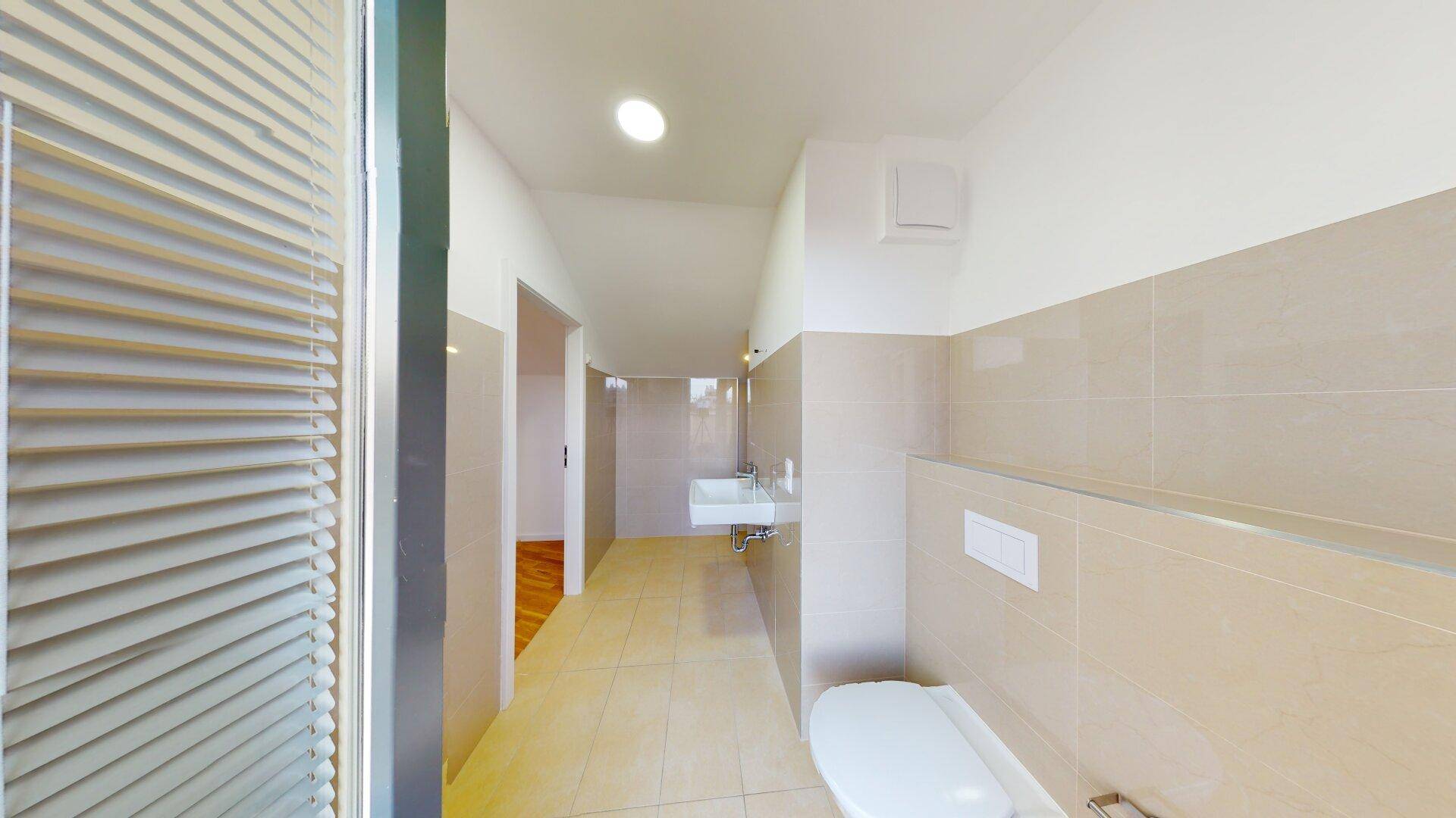 Modernes WC mit hellen Fliesen, wandhängendem WC und Waschbecken in neuwertigem Zustand.
