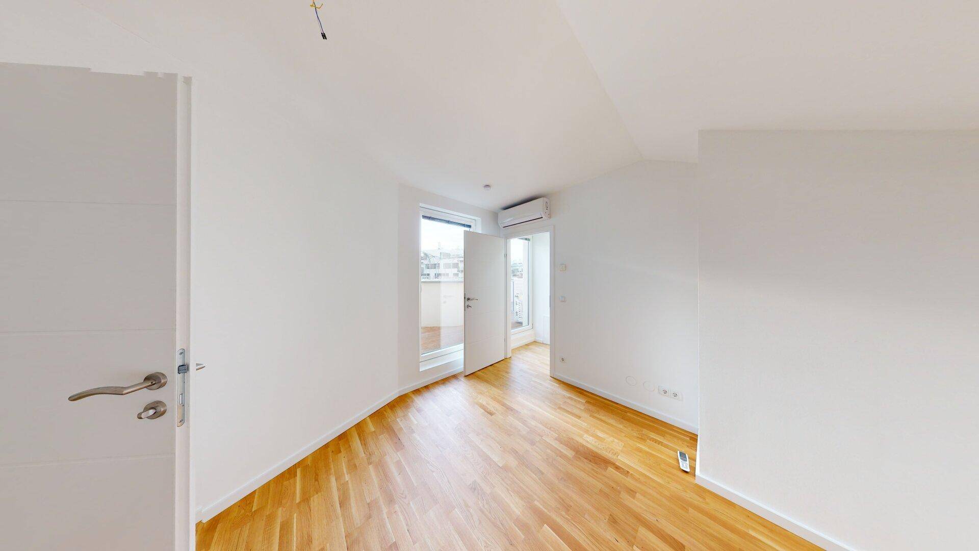 Helles Zimmer mit Echtholzparkett, weißen Wänden und Zugang zu einem Balkon.