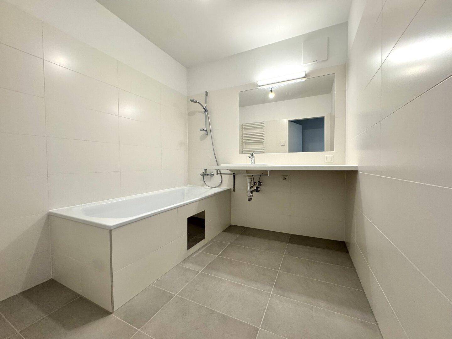 Modernes Badezimmer mit Badewanne, Einzelwaschbecken und hellen Fliesen an Wänden und Boden.