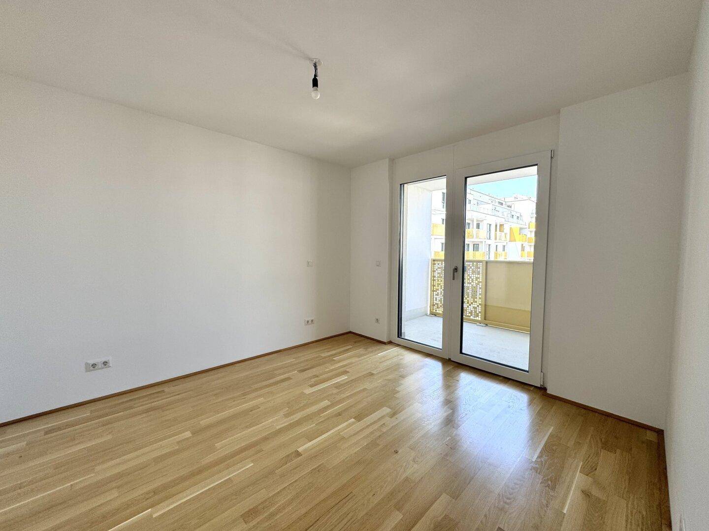 Helles Schlafzimmer mit Parkettboden und direktem Zugang zu einem kleinen Balkon.