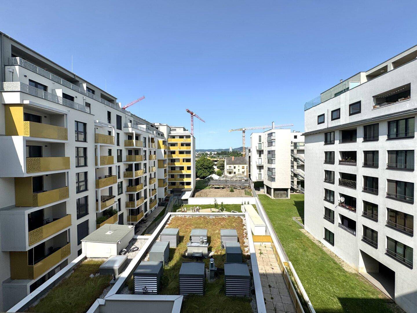 Blick auf moderne Wohngebäude mit begrünten Dächern und Baustellen in der Umgebung.