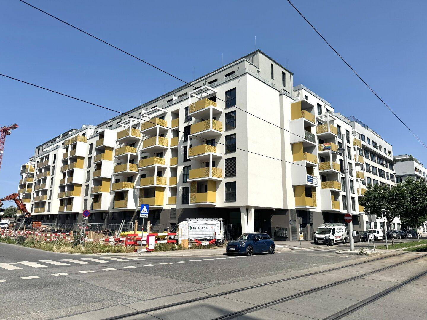 Moderne Wohngebäude an einer belebten Straße mit Straßenbahnschienen und Baustellenaktivität.