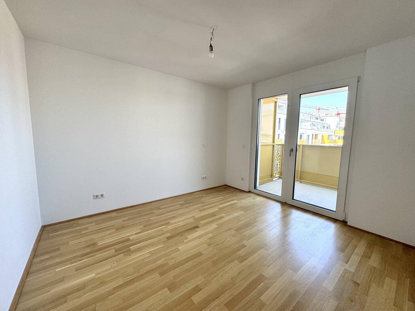 Helles, leeres Zimmer mit Parkettboden und großem Zugang zu einem Balkon, ideal als Schlafzimmer.