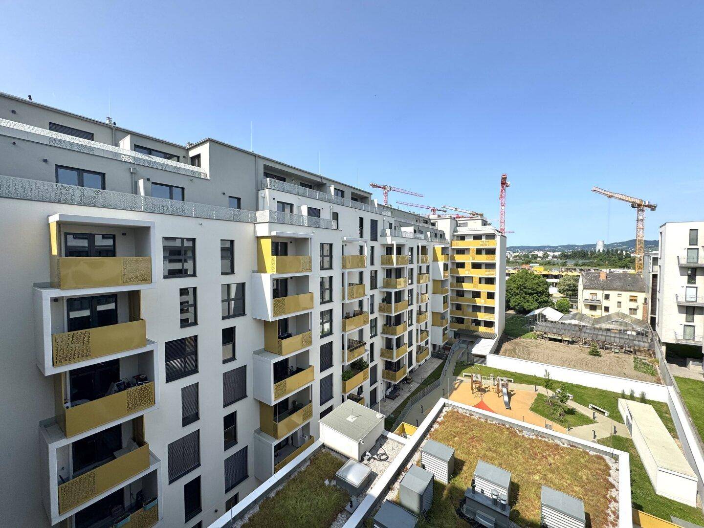 Moderne Wohngebäude mit zahlreichen Balkonen und begrünten Dächern unter blauem Himmel.