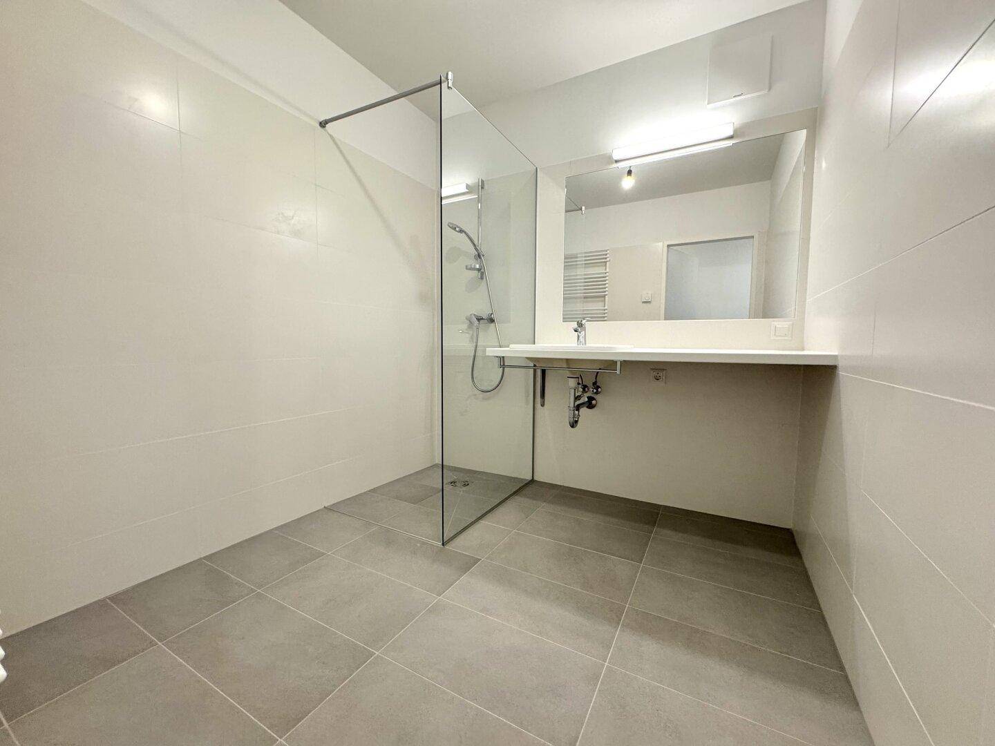 Modernes Badezimmer mit begehbarer Dusche, grauen Bodenfliesen und einem einzelnen Waschbecken.