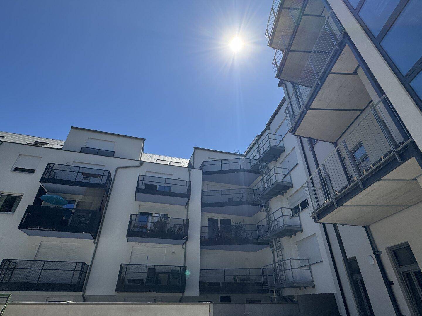 Moderne Wohnanlage mit zahlreichen Balkonen und viel Glas unter strahlendem Himmel.