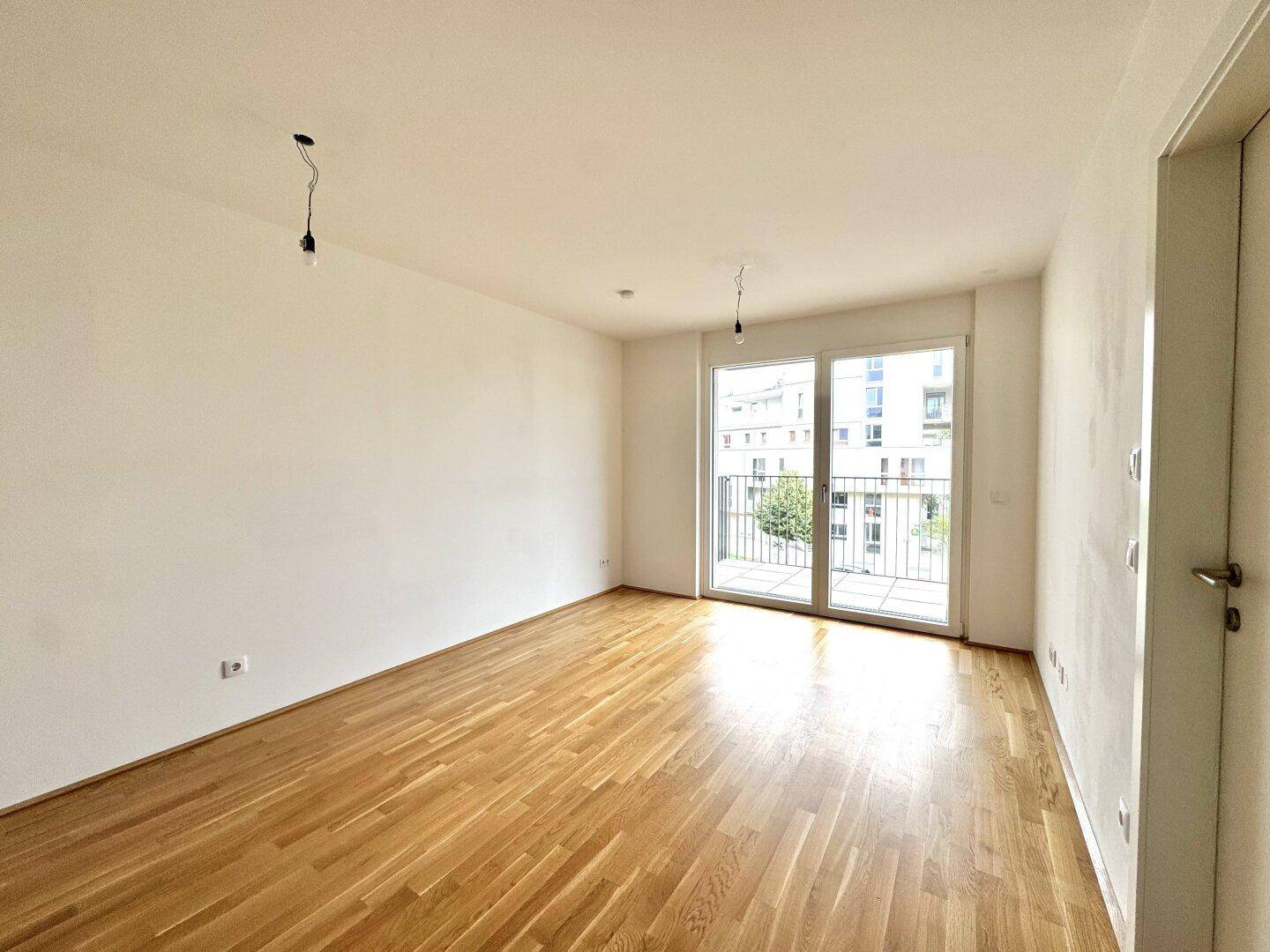 Heller, leerer Raum mit Holzboden und Zugang zu einem Balkon durch eine große Glastür.