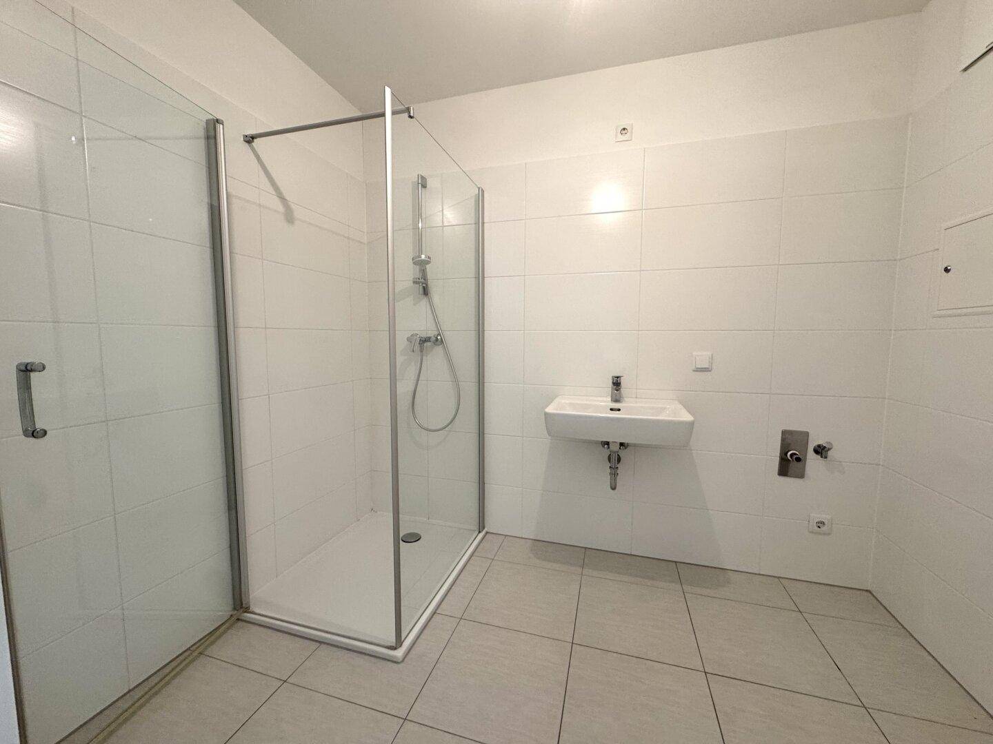 Modernes Badezimmer mit weißen Fliesen, einer begehbaren Dusche und einem einzelnen Waschbecken.