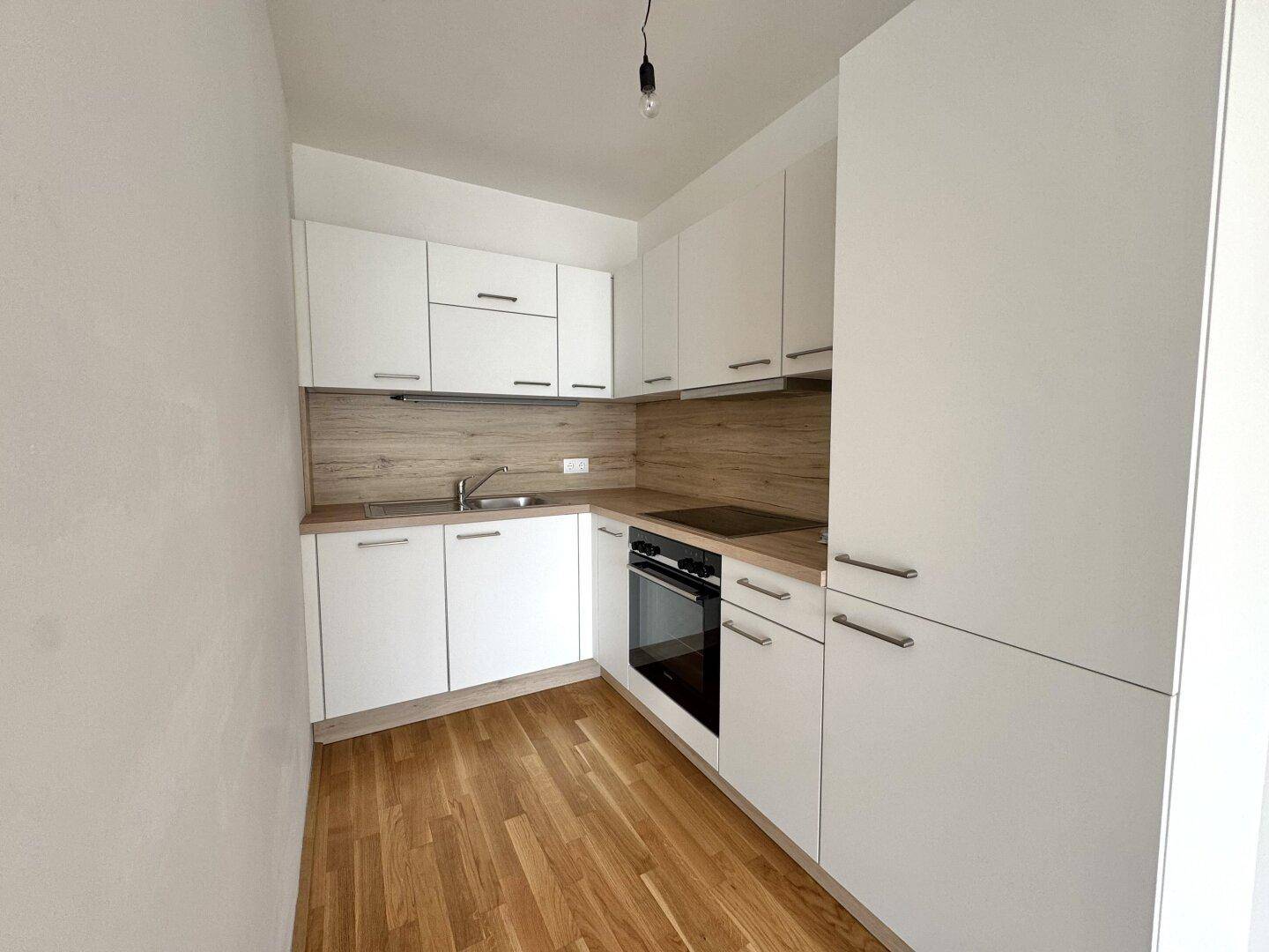 Moderne Küchenzeile mit weißen Schränken, Holzoptik-Arbeitsplatte und integriertem Backofen.