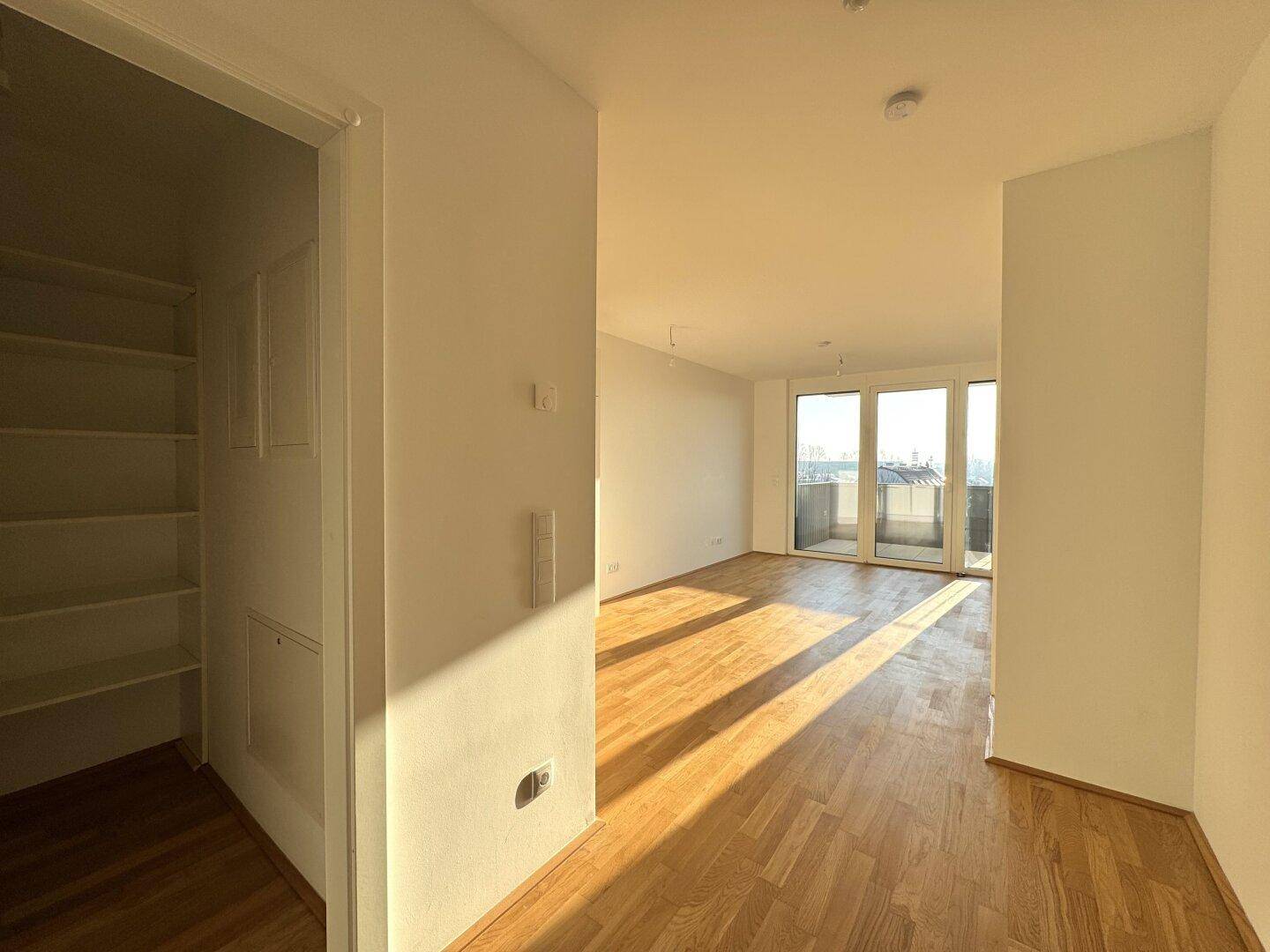 Lichtdurchfluteter Wohnbereich mit Parkettboden, Zugang zum Balkon und praktischer Abstellnische.