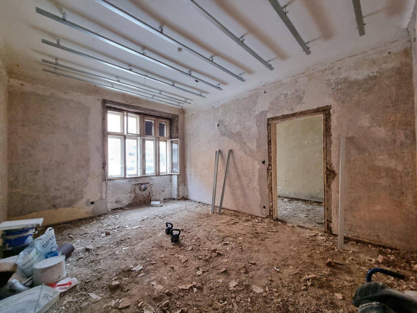 Raum in Renovierung mit abgenutzten Wänden, Schutt auf dem Boden und Deckenkonstruktion.
