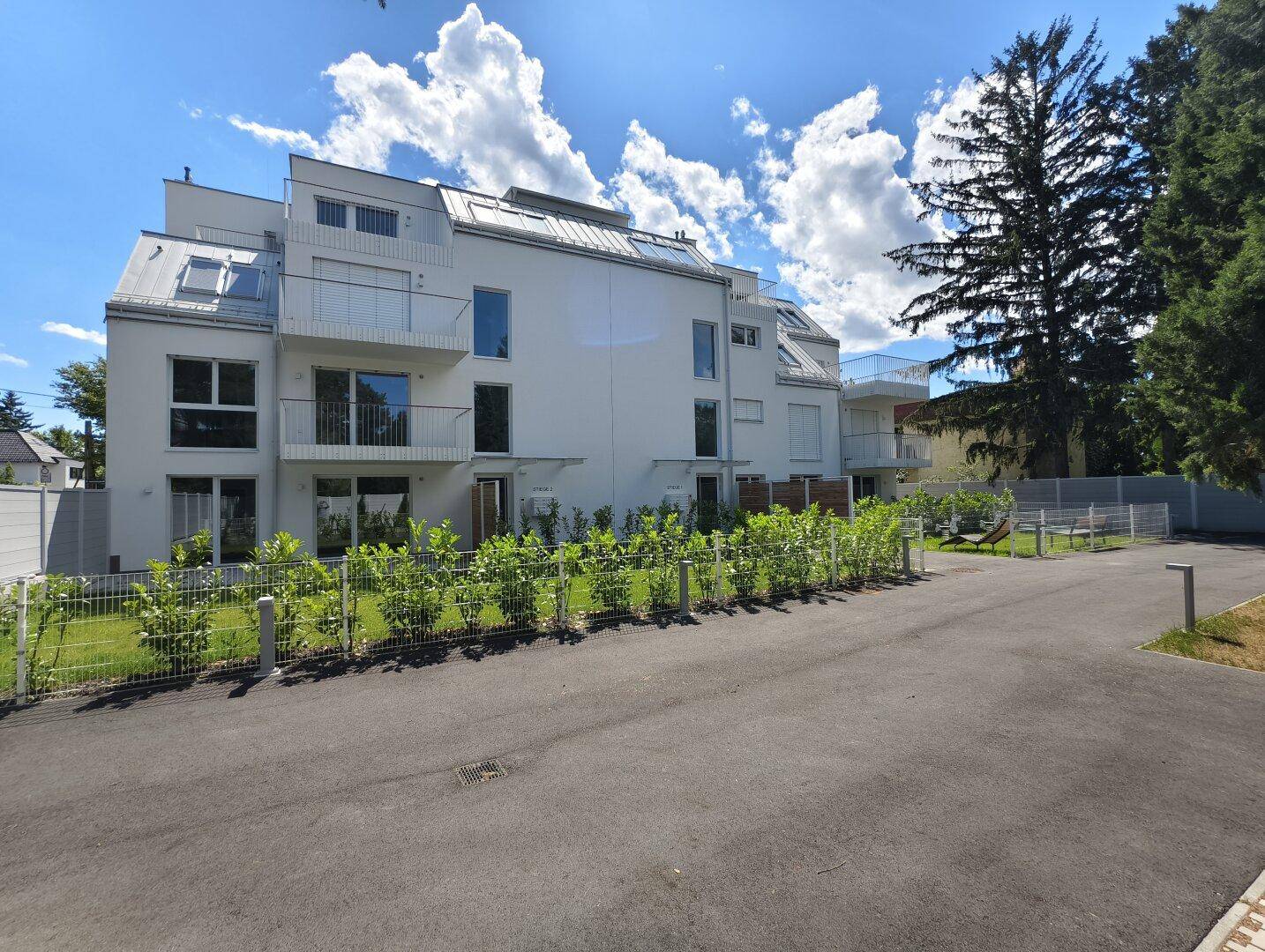 Seitenansicht des modernen Gebäudes von der Straße aus, umgeben von Bäumen und Grünflächen.
