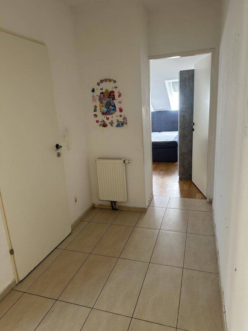 Schmaler Flur mit Fliesenboden, Heizkörper und Blick in ein angrenzendes Schlafzimmer.