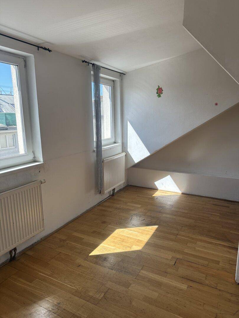 Heller Raum im Dachgeschoss mit Holzboden, zwei Fenstern und schrägen Wänden.