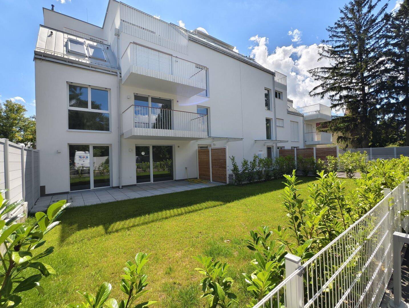 Moderne Wohnanlage mit gepflegtem Garten und Balkonen unter blauem Himmel.
