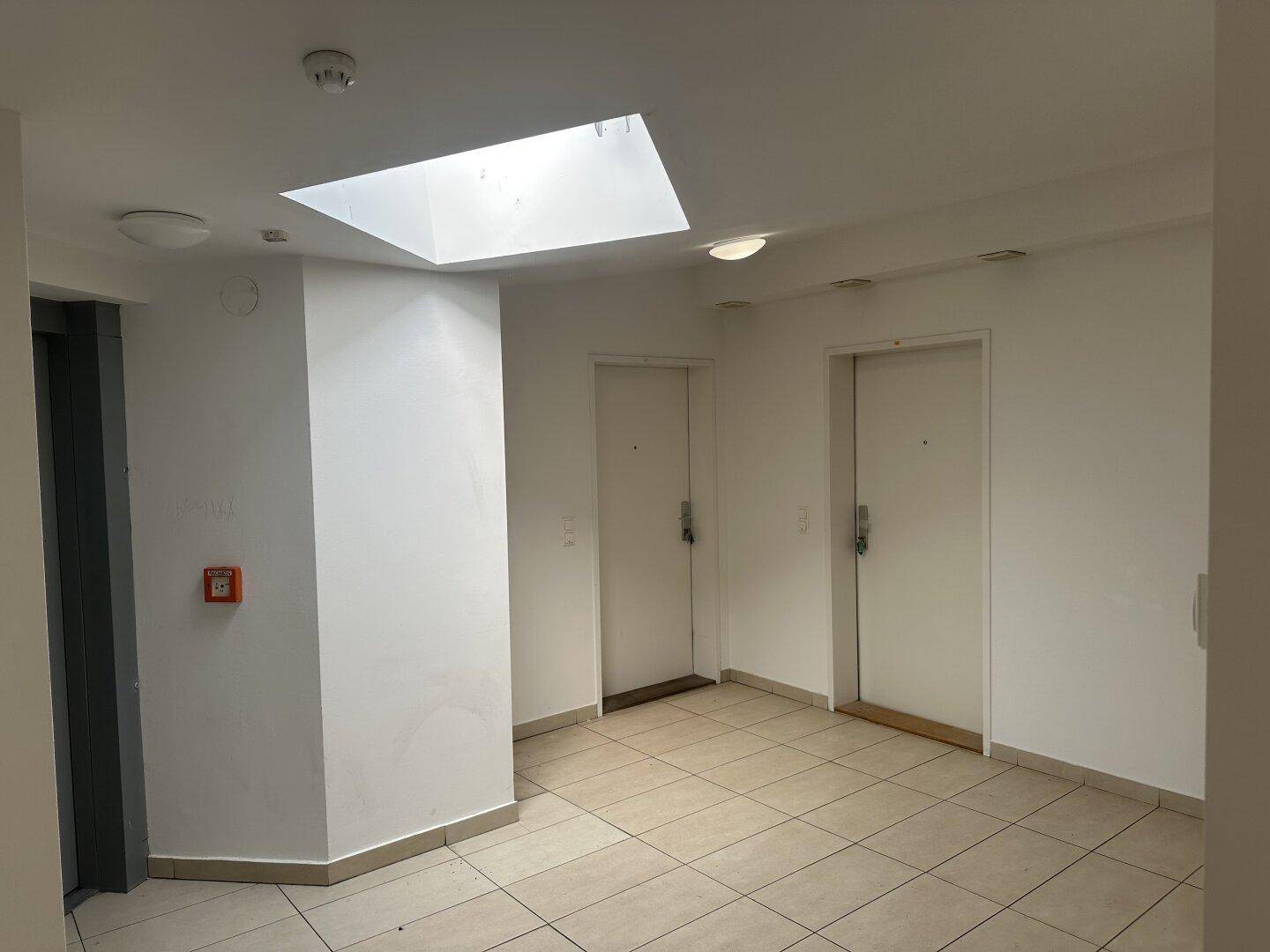 Heller Flur mit Fliesenboden, Oberlicht und Zugang zu den Wohnungen sowie einem Aufzug.