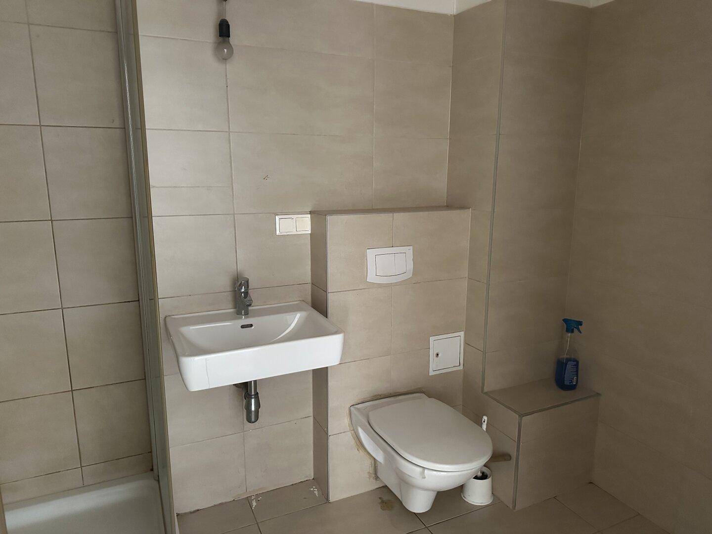 Modern gefliestes Badezimmer mit Dusche, wandhängendem WC und Einzelwaschbecken.