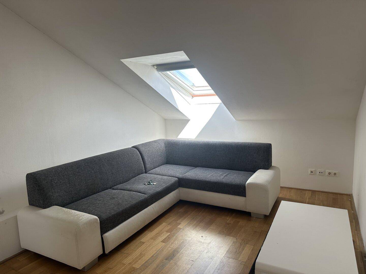 Gemütliches Wohnzimmer im Dachgeschoss mit Ecksofa, Holzboden und einem hellen Dachfenster.