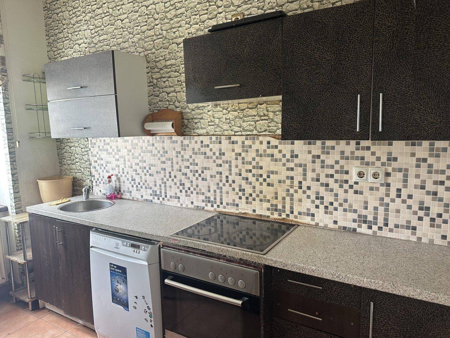 Kleine Küche mit dunklen Schränken, Mosaikfliesen und integrierten Geräten.